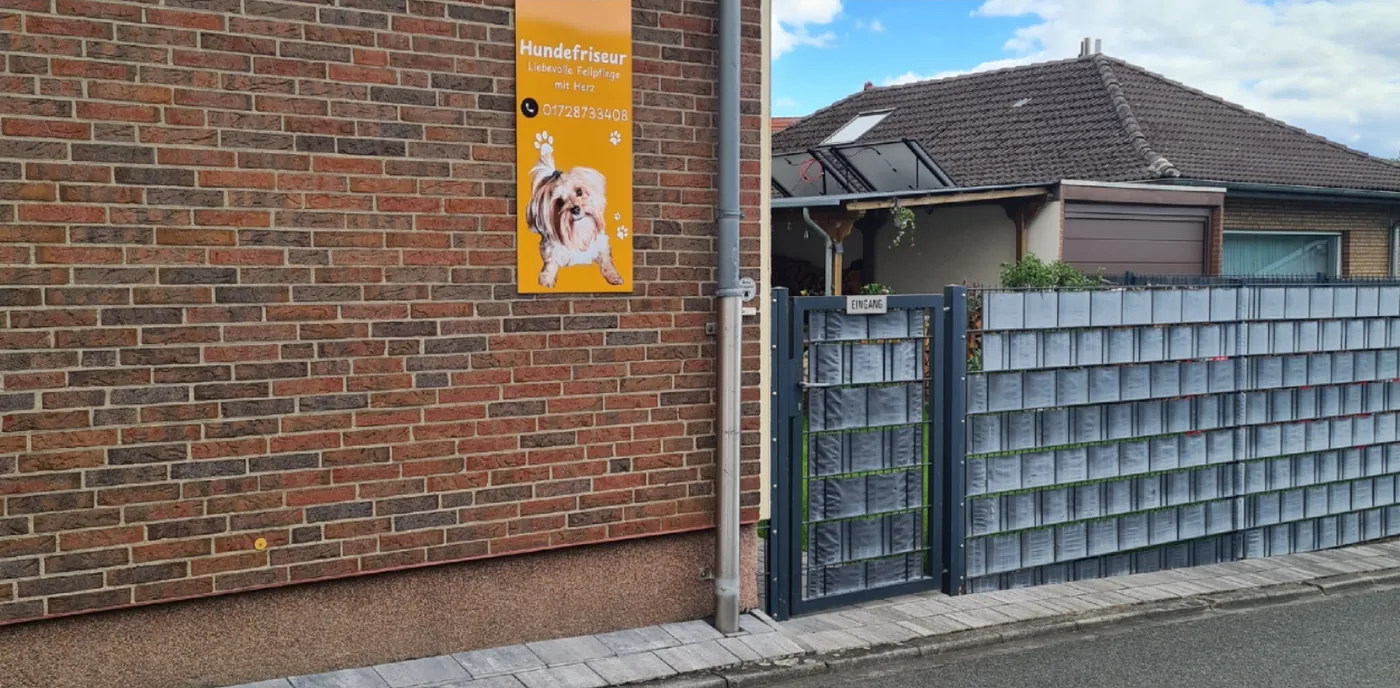 Schild des Hundefriseurs Monika Beyer an der Hauswand, daneben der Eingang zum Salon in Hilter